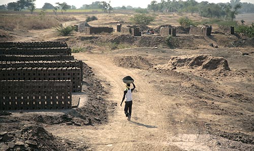 Person walking through dusty land carrying work materials on their head